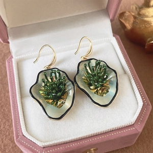 Macro shot of green enamel flower earrings in a pink velvet jewelry box with gold trim