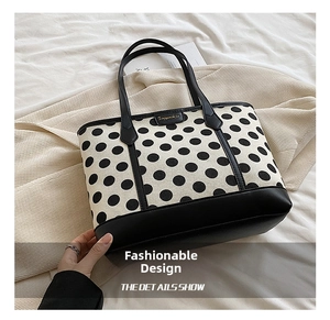 Close-up of a polka dot tote bag with canvas body, leather handles, and metal logo plaque
