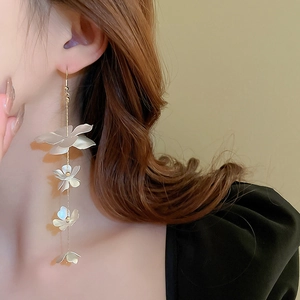 Macro view of long gold chain earrings featuring white matte layered flower charms