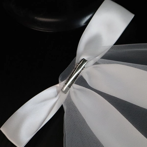 Detail of white satin bow with metal alligator clip and sheer mesh veil fabric