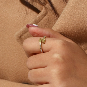 Detail of adjustable gold ring with hugging hands design and zircon stones on model's finger