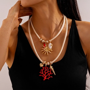 Detail of layered sun pendant and red coral charm necklace with beige cord