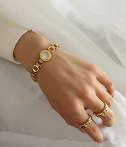 Detail of Roman numeral bangle and twisted rope ring on white textured fabric