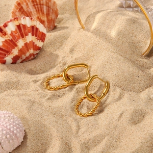 Close-up of golden twist rope hoop earrings placed on beach sand with sea shells
