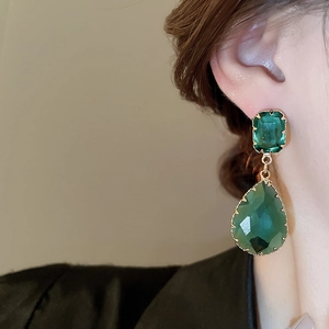 Close-up of elegant gold drop earrings with emerald green square and teardrop stones
