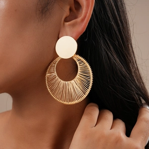 Close-up of model wearing hollow circular twisted gold earrings with woven wire detail