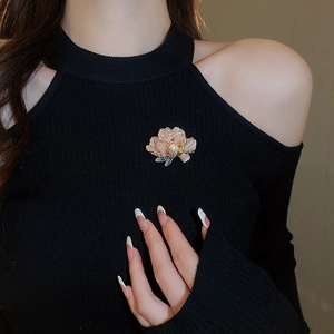 Detail of pink floral brooch with pearl on a black knit shoulder-off top