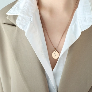 Collier doré minimaliste avec pendentif visage abstrait porté sur un blazer élégant