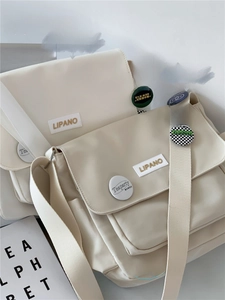 Comparison of cream canvas messenger bags in two sizes with decorative pins and labels