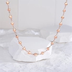 Detailed close-up of rose gold heart-shaped link necklace on a white stone pedestal