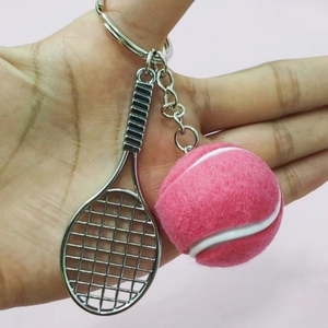 Detail of pink felt tennis ball and silver metal racket keychain held against pink wall