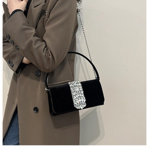 Detail of black velvet evening bag featuring a sparkling rhinestone buckle and metal chain