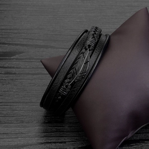 Close-up of black braided multi-layer leather bracelet with dark metal feather charm