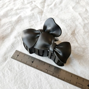 Detail shot of a matte black double bow hair claw clip measuring 8.5cm on a scale