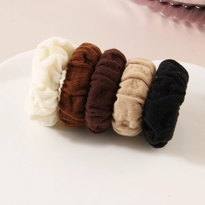 Five-piece set of knitted elastic hair scrunchies in neutral earth tones on a white plate