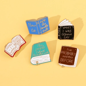 Detailed view of five creative book-shaped enamel brooches with witty quotes on yellow background