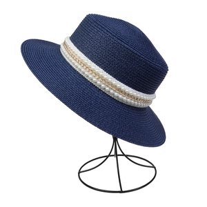 Detail of dark blue straw sun hat featuring elegant white pearls and gold chain band