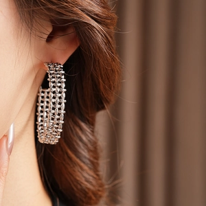 Close-up of wide silver open hoop earrings with intricate woven texture on female model