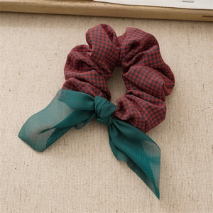 Detail of red and black plaid hair scrunchie with green sheer tulle bow on beige fabric