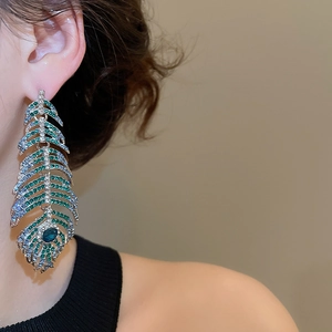 Detailed view of silver peacock feather earrings with emerald green and blue crystals