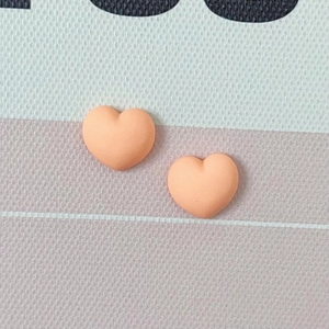 Deux petits charms en forme de cœur en résine orange mat sur fond de tissu texturé