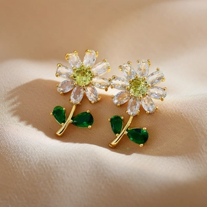 Gold plated green flower earrings with sparkling cubic zirconia on beige fabric