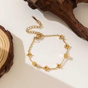 Detailed shot of a gold four-leaf clover and cube charm bracelet on wooden props
