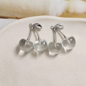Close-up of translucent cherry pendants with silver stems on a light ceramic plate