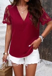 Close-up of red V-neck top with intricate lace patchwork sleeves and white denim shorts