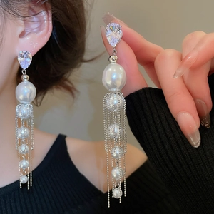 Détail de boucles d'oreilles avec goutte en cristal, perle blanche et franges argentées