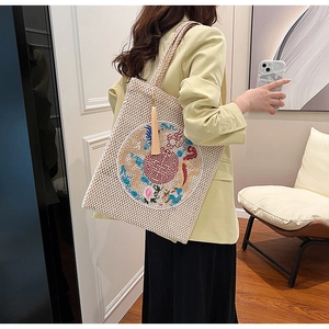 Detail view of woven straw tote bag with traditional Chinese embroidery and tassels
