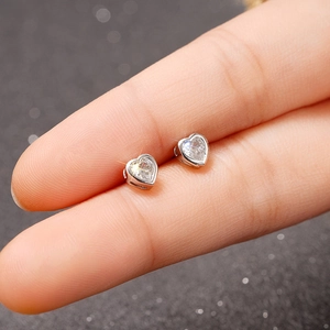 Macro view of small silver heart stud earrings with heart-shaped zircon on a finger