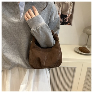Braune Falten-Halbmondtasche mit Kette, präsentiert an der Schulter in warmer Kulisse