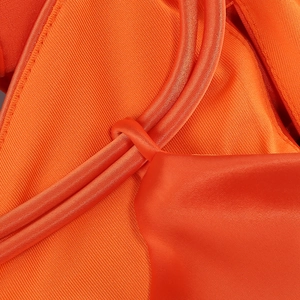 Detailed close-up of bright orange halter dress fabric texture with intricate stitching