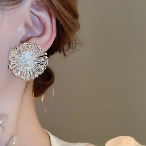 Detail of silver flower stud earring with pearl center and intricate metal petals on ear