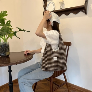 Brown and beige plaid knit tote bag shown from a side view in a cozy indoor setting