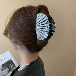 Detail view of a large silver metal shell claw clip for a stylish hair bun hairstyle