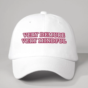 Detailed close-up of pink 'VERY DEMURE' embroidery on a white cotton baseball cap