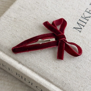 Detail shot of a dark red velvet bow hair clip on an ivory book with silver metal base