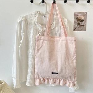 Detail of pink canvas tote bag showing striped texture, ruffle edge, and brand label