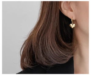 Close-up of golden 3D heart-shaped pendant earrings on a model with metallic finish
