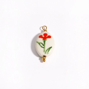 Close-up of white ceramic oval pendant with red floral patterns and 18K gold accents