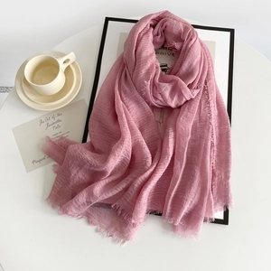 Detailed texture of dusty pink cotton linen scarf with natural raw edges on a white desk