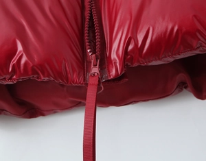 Detail of red glossy puffer jacket featuring a matching plastic zipper and ribbed pull tab