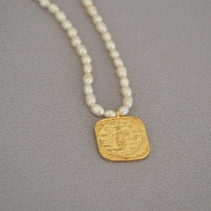 Detailed close-up of a gold square medallion pendant with relief on a white pearl necklace