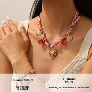 Gros plan sur parure bijoux foulard en soie avec pendentifs cœur et soleil dorés