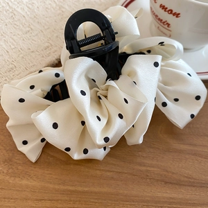 Detail of white polka dot fabric bow on a black claw hair clip atop a wooden surface