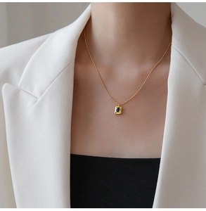 Detailed view of square gold necklace with green gemstone worn on white blazer