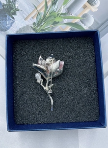 Detailed back view of a silver magnolia brooch with pink petals in a gift box