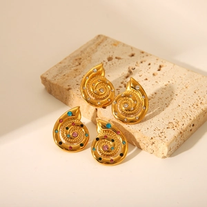 Detailed shot of gold shell earrings with clear and colorful zircon on a stone